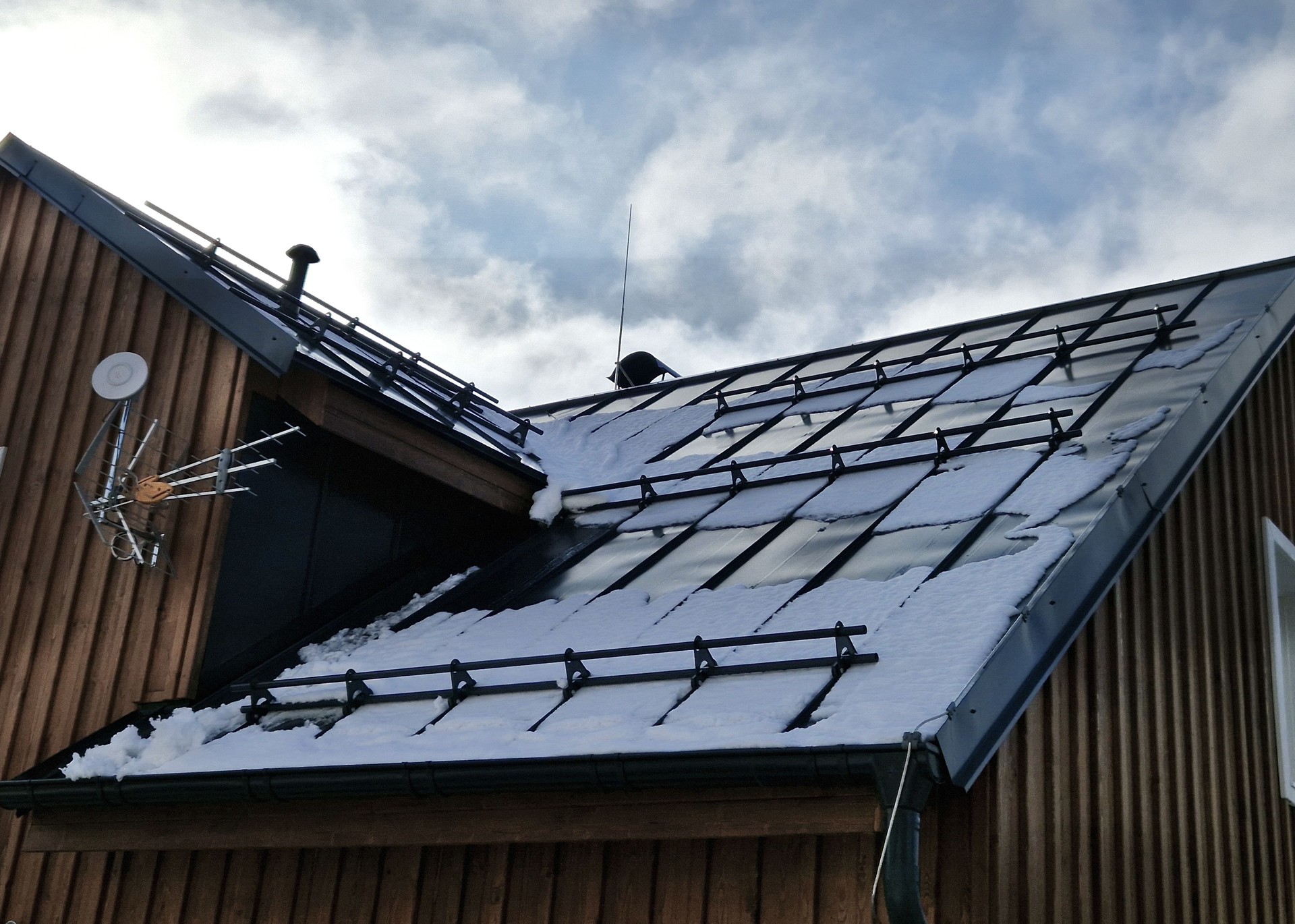 galvanized metal roof in mountains with a bar against rapid sliding of snow. If snow and ice quickly fall on people under roof, they will be injured or dead. slows down avalanche, injury head, broken